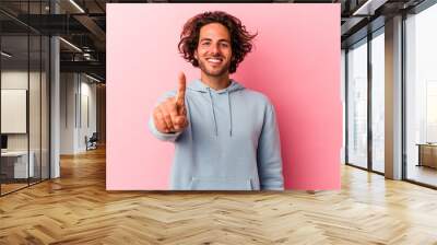 Young caucasian man isolated on pink bakcground showing number one with finger. Wall mural