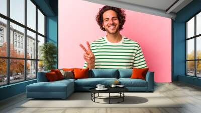 Young caucasian man isolated on pink bakcground showing victory sign and smiling broadly. Wall mural