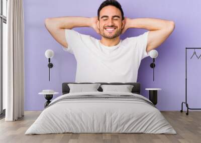 Young caucasian man isolated on purple background feeling confident, with hands behind the head. Wall mural