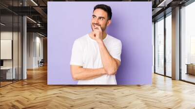 Young caucasian man isolated on purple background relaxed thinking about something looking at a copy space. Wall mural