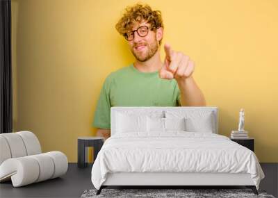 Young caucasian man isolated on yellow background cheerful smiles pointing to front. Wall mural