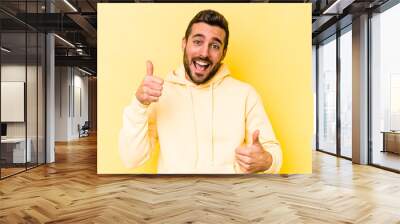 Young caucasian man isolated on yellow background raising both thumbs up, smiling and confident. Wall mural