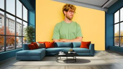 Young caucasian man isolated on yellow background suspicious, uncertain, examining you. Wall mural