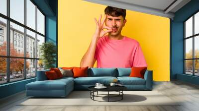 Young caucasian man isolated on yellow background with fingers on lips keeping a secret. Wall mural