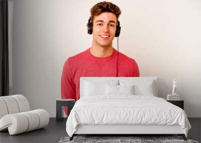 Young caucasian man listening to music isolated on white background happy, smiling and cheerful. Wall mural