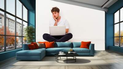 Young caucasian man sitting on the floor holding on laptop isolated on white background who is bored, fatigued and need a relax day. Wall mural