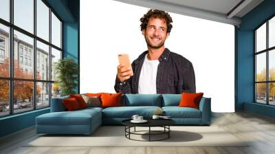 Young caucasian man using mobile phone isolated looks aside smiling, cheerful and pleasant. Wall mural