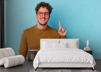 Young caucasian man wearing eyeglasses isolated on blue background showing number one with finger. Wall mural