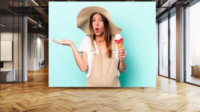 Young caucasian pregnant woman holding an ice cream isolated on blue background surprised and shocked. Wall mural