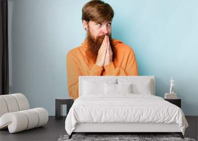 Young caucasian red-haired man isolated on blue background praying, showing devotion, religious person looking for divine inspiration. Wall mural