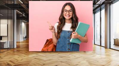 Young caucasian student woman isolated on pink background smiling and pointing aside, showing something at blank space. Wall mural