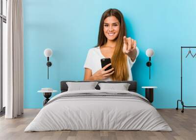 Young caucasian woman holding a phone cheerful smiles pointing to front. Wall mural