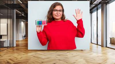 Young caucasian woman holding battery box isolated on blue background smiling cheerful showing number five with fingers. Wall mural