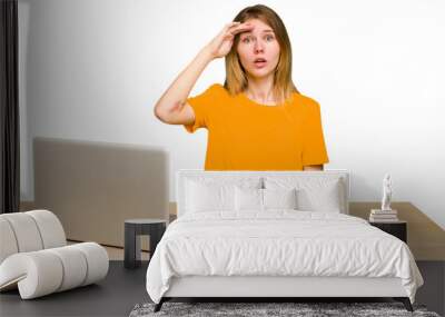 Young caucasian woman in a workplace working with a laptop isolated shouts loud, keeps eyes opened and hands tense. Wall mural