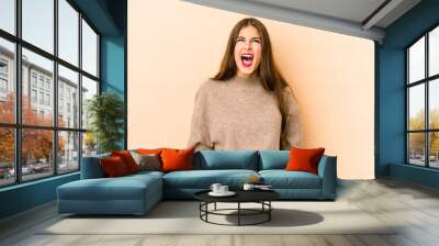 Young caucasian woman isolated en beige background shouting very angry, rage concept, frustrated. Wall mural