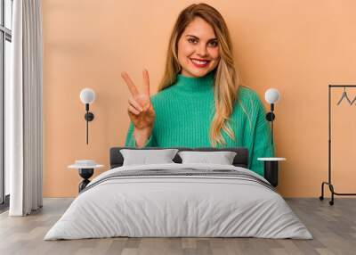 Young caucasian woman isolated on beige background joyful and carefree showing a peace symbol with fingers. Wall mural