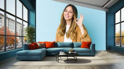 Young caucasian woman isolated on blue background cheerful and confident showing ok gesture. Wall mural