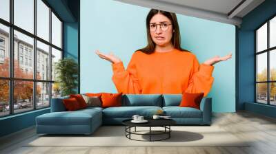 Young caucasian woman isolated on blue background confused and doubtful shrugging shoulders to hold a copy space. Wall mural