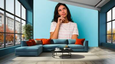 Young caucasian woman isolated on blue background relaxed thinking about something looking at a copy space. Wall mural