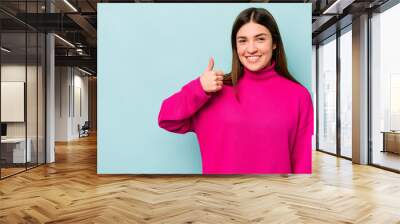 Young caucasian woman isolated on blue background smiling and raising thumb up Wall mural