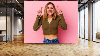 Young caucasian woman isolated on pink background crossing fingers for having luck Wall mural