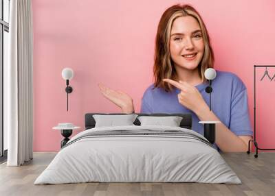 Young caucasian woman isolated on pink background excited holding a copy space on palm. Wall mural