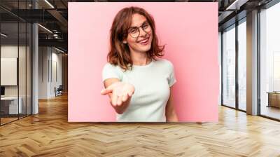 Young caucasian woman isolated on pink background stretching hand at camera in greeting gesture. Wall mural