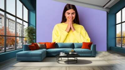 Young caucasian woman isolated on purple background holding hands in pray near mouth, feels confident. Wall mural