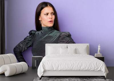 Young caucasian woman isolated on purple background looks aside smiling, cheerful and pleasant. Wall mural