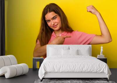 Young caucasian woman isolated on yellow background showing strength gesture with arms, symbol of feminine power Wall mural