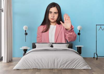 Young Caucasian woman on blue backdrop standing with outstretched hand showing stop sign, preventing you. Wall mural