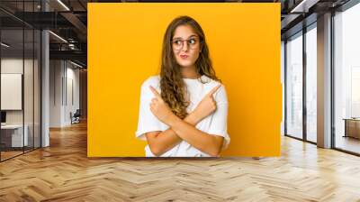 Young caucasian woman points sideways, is trying to choose between two options. Wall mural