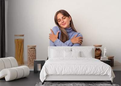 Young caucasian woman sitting at a table with food pot isolated on white background hugs, smiling carefree and happy. Wall mural