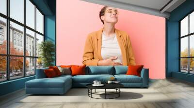 Young caucasian woman wearing a casual business clothes touches tummy, smiles gently, eating and satisfaction concept. Wall mural