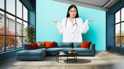 Young chinese doctor woman confused and doubtful shrugging shoulders to hold a copy space. Wall mural