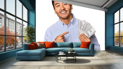 Young Chinese man holding dollar bills in studio smiling and pointing aside, showing something at blank space. Wall mural