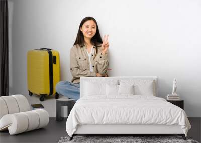 Young chinese traveler woman sitting holding a boarding passes showing number two with fingers. Wall mural