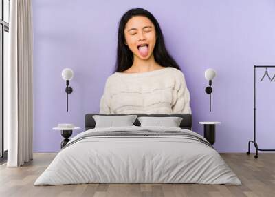 Young chinese  woman isolated on a purple background funny and friendly sticking out tongue. Wall mural