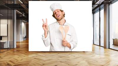 Young cook man isolated on white background joyful and carefree showing a peace symbol with fingers. Wall mural