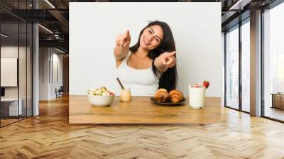 Young curvy woman taking a breakfast cheerful smiles pointing to front. Wall mural