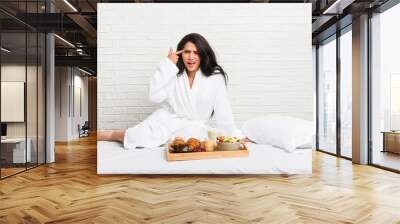 Young curvy woman taking a breakfast on the bed showing a disappointment gesture with forefinger. Wall mural