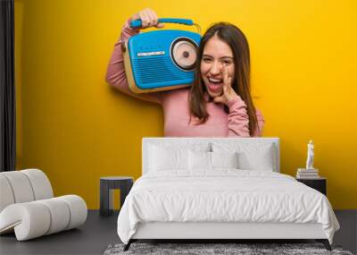 Young cute woman holding a vintage radio shouting something happy to the front Wall mural