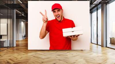 Young delivery caucasian man holding pizzas isolated on white background joyful and carefree showing a peace symbol with fingers. Wall mural