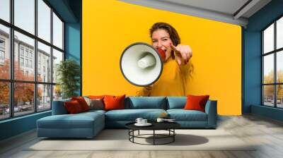 Young european woman holding a megaphone cheerful smiles pointing to front. Wall mural