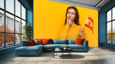 Young european woman holding a spanish flag looking sideways with doubtful and skeptical expression. Wall mural