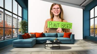 Young gardener woman holding a plan based placard isolated on white background happy, smiling and cheerful. Wall mural