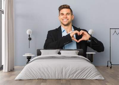 Young handsome caucasian man smiling and showing a heart shape with hands. Wall mural