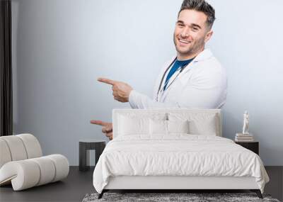 Young handsome doctor man excited pointing with forefingers away. Wall mural