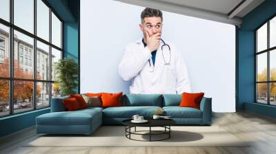 Young handsome doctor man thoughtful looking to a copy space covering mouth with hand. Wall mural