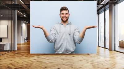 Young handsome fitness man makes scale with arms, feels happy and confident. Wall mural